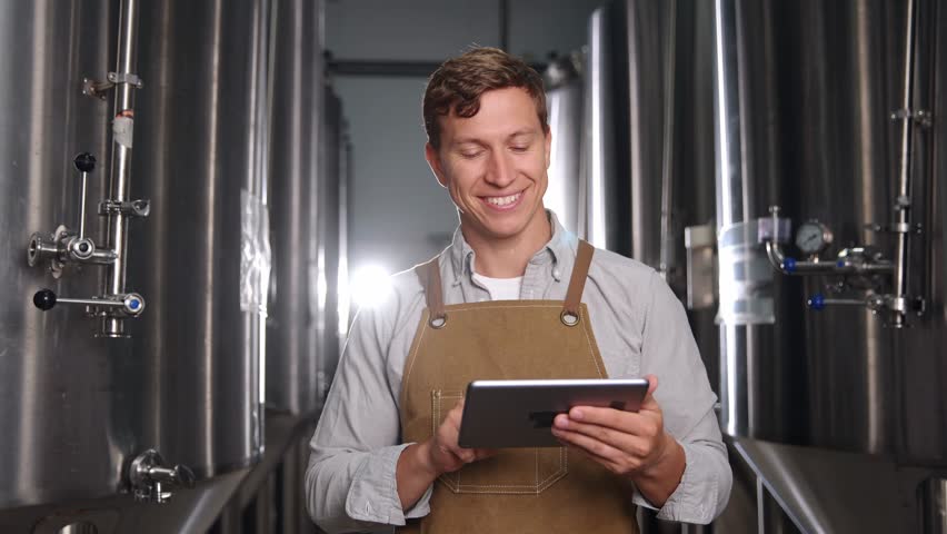 Portrait worker man on food factory, Smiling brewer utilizing tablet in modern brewery production process.