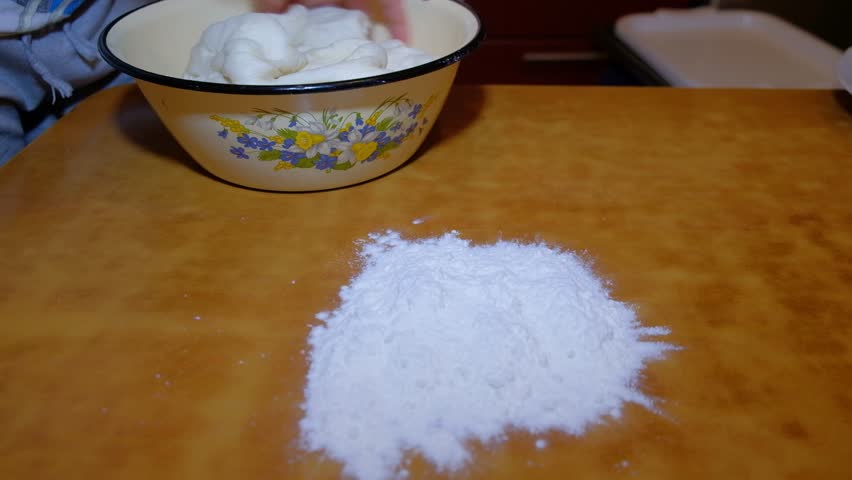 woman in apartment at home kneading dough to make pizza, human hands visible product all actions on table dark color kneading dough with two hands and one