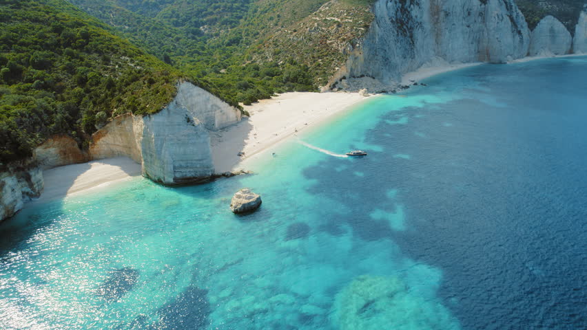 Speedboat passing near white cliffs and sandy beach with turquoise sea in Kefalonia Greece