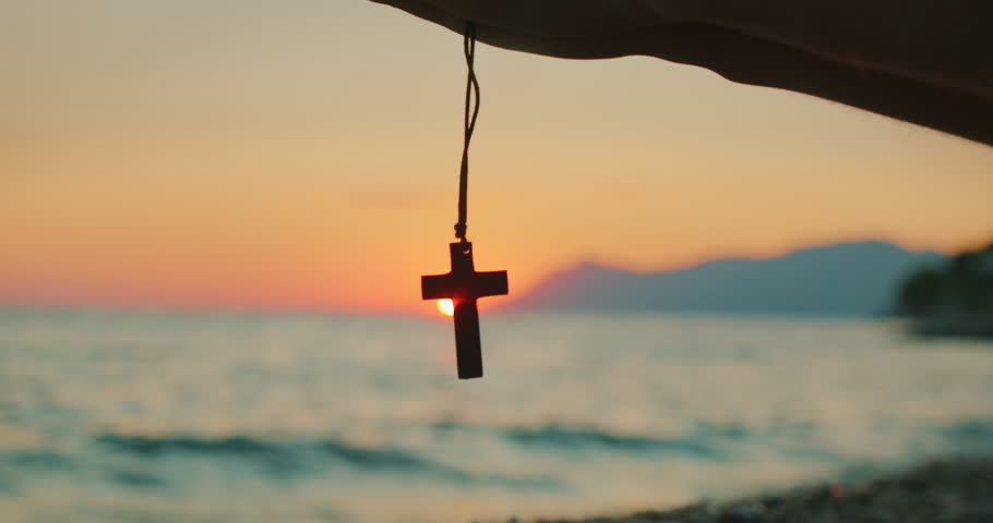 Wooden cross pendant held up at sunset over the Adriatic Sea in summer Croatia