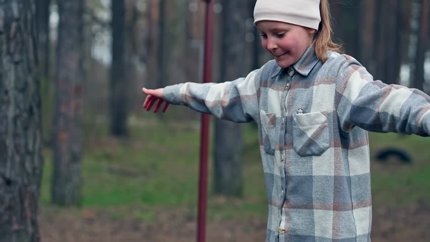 Slowmo of Caucasian schoolgirl doing gymnastics at the playground in the forest park standing on the bar and trying to keep balance. Cute laughing female kid is walking on nature at autumn day