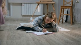 Thoughtful schoolgirl is doing homework and erasing mistakes in copybook lying on the floor. Cute Caucasian child is writing and solving mathematics problems. She is studying school subjects at home - Powered by Shutterstock - Get 15% off with code: PIKWIZARD15