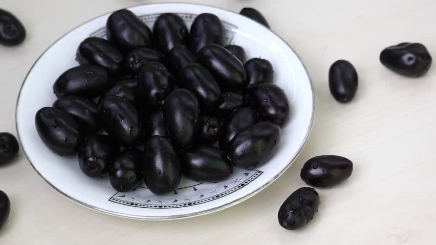 Fresh Black Plums on white plate, also known as Jamun, Java Plum, Malabar Plum, Jambolan. Syzygium cumini fruit, perfect for healthy eating and natural produce visuals.