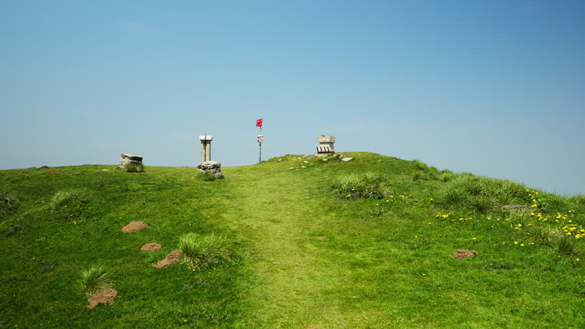 Scenic summit of Golica in Slovenia with grassy peak, waypoint marker, scattered rocks, and deep blue sky on a warm, peaceful summer day in the mountains.