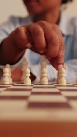 Vertical video,A dark-skinned person sets up white chess pieces on a chessboard in a medium close-up shot. They carefully position each piece, ready to start a game.