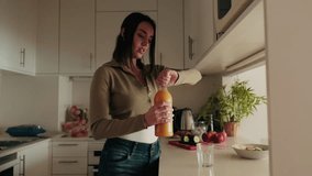 A young woman pours herself a glass of orange juice in her modern kitchen. She is wearing casual clothes and has a healthy lifestyle. - Powered by Shutterstock - Get 15% off with code: PIKWIZARD15