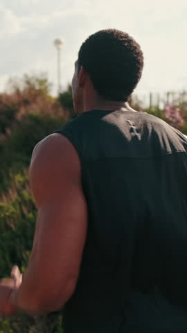 Vertical video, A young athletic male runs outdoors on a sunny day. He is focused, determined, and working towards his fitness goals.