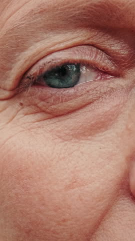 Vertical video, Close-up of a senior woman's face, highlighting her expressive blue eyes and the wrinkles that tell a story of a life well-lived.