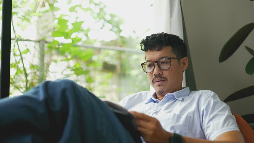 Asian man peacefully reading a book by the window.4k