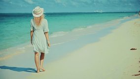 lone woman in a white dress and straw hat walks barefoot along a pristine sandy beach, gazing out at the vast turquoise ocean under a clear sky, embodying tranquility and vacation - Powered by Shutterstock - Get 15% off with code: PIKWIZARD15