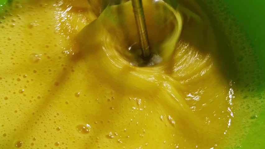 yellow of raw eggs being vigorously whisked with an electric mixer, creating a bubbly and frothy texture, likely for a baking recipe. Kneading Dough With Whisk For Baking Cake. Chef Cook Dessert