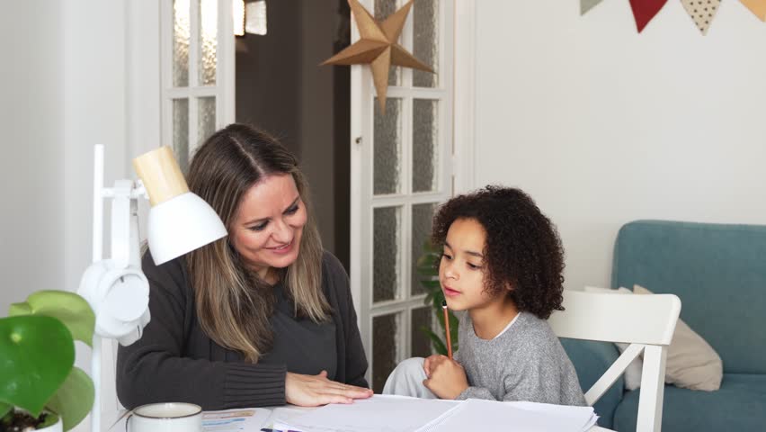 Caucasian mother and African American daughter studying at home, doing homework in cosy white room. Parent teach, child school girl learn knowledge, write exercise read book. Education for children