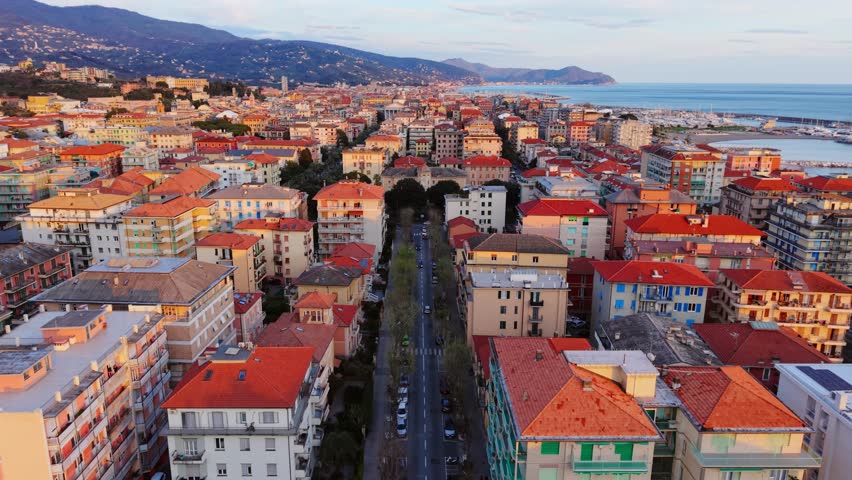 Coastal italian city with sea, sunset light, and mountain backdrop, aerial view