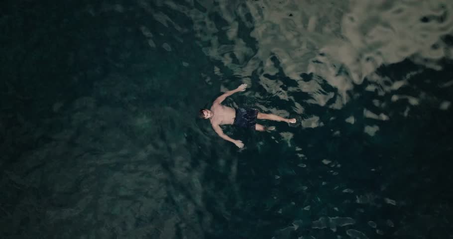 Top-down aerial of a man floating still in deep volcanic waters, surrounded by gentle ripples and soft reflections in Seixal.