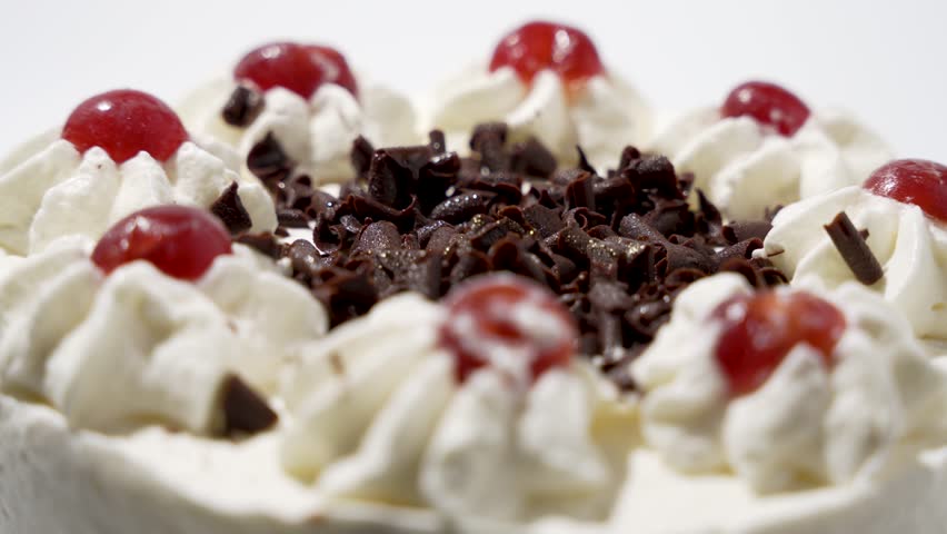 Chocolate shavings in close-up on cake. Central focus on the rotating chocolate shavings on cream. The contrast between the dark chocolate and the white cream creates a particularly elegant effect.