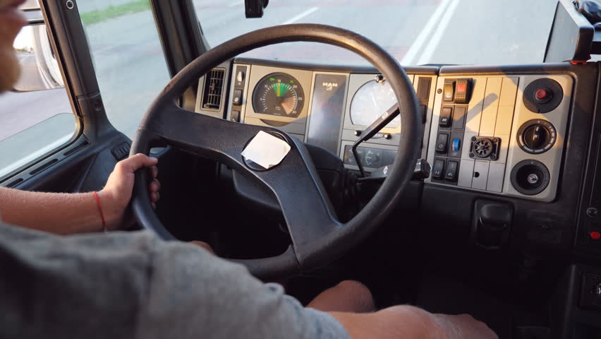 Unrecognizable man holding his hand on steering wheel and driving truck at urban road. Lorry driver rides to destination. View from inside of the car cab. Back view Slow motion Close up