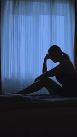 black silhouette upset unhappy woman sitting on bed dark room mood depression sadness emotion. Sad lonely Girl feels bad after party, insomnia migraine suffers headache. window curtains vertical video