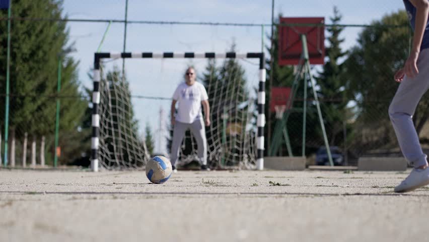 Young boy practicing soccer shooting with father as goalkeeper outdoors