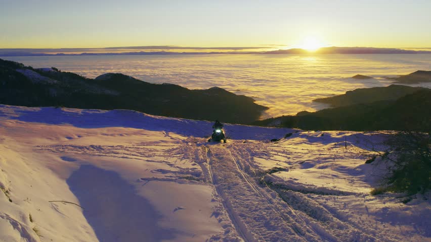 Snowmobile adventure on mountain high altitude with sunset scenic snowy landscape and fog covered valley at background