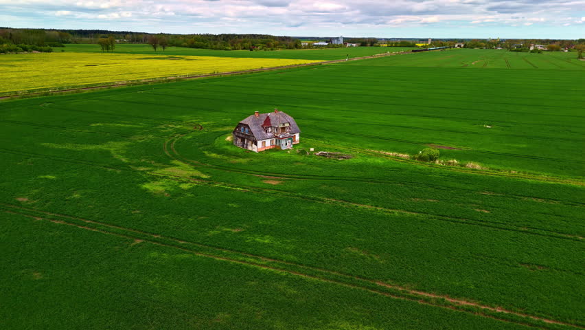 Decrepit home sits in wide empty field surrounded by patchy grass