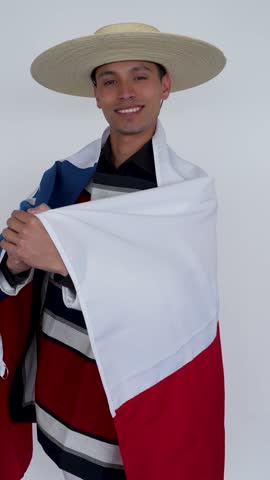 Young happy smiling chilean man wearing traditional Huaso blanket and hat showing chilean flag isolated on white background, Fiestas Patrias Chile celebration