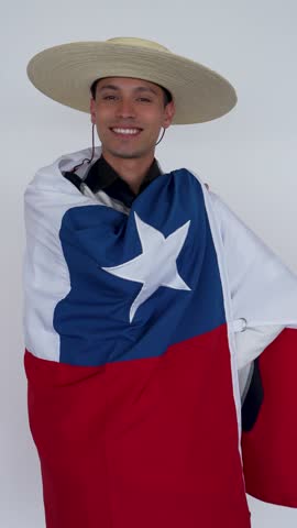 Young happy smiling chilean man wearing traditional Huaso blanket and hat showing chilean flag isolated on white background, Fiestas Patrias Chile celebration