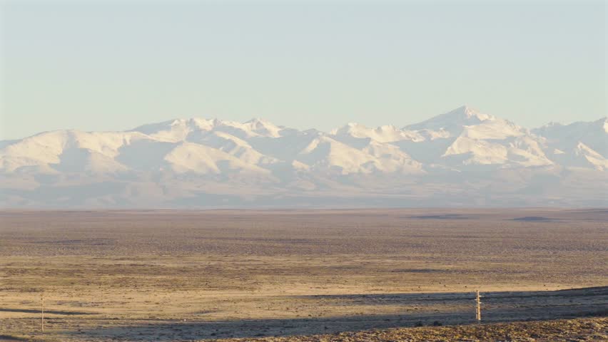 Drone shows Argentina’s legendary Route 40 stretching across the Patagonian plain with the Andes towering in the background under golden evening light,