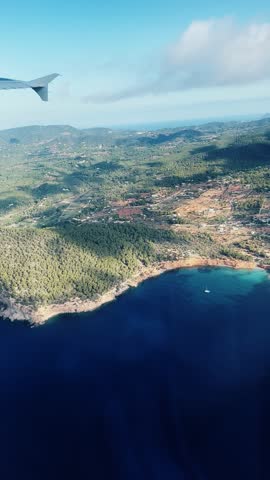 Passenger pov from plane landing in Ibiza island, Spain with forested coastline and blue ocean water, vertical video