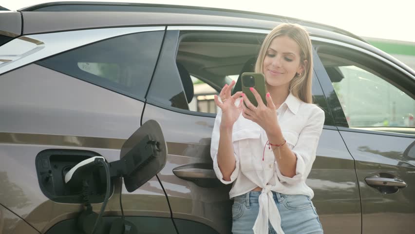 Young woman using her smartphone while her electric vehicle is charging
