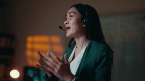 Young professional Asian woman wearing headset, communicating remotively from stylish home office during evening hours, engaging in business conversation with confident demeanor - Powered by Shutterstock - Get 15% off with code: PIKWIZARD15