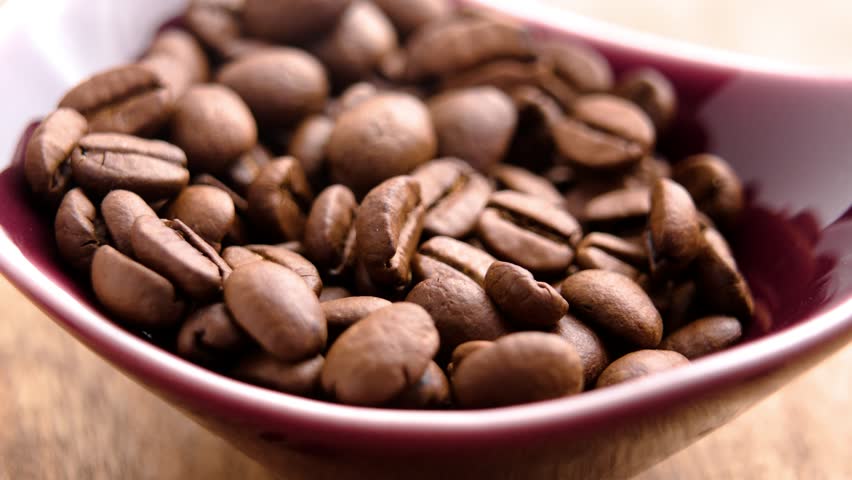 Bamboo spoon scooping organic roasted coffee beans from a red ceramic bowl. Macro shot