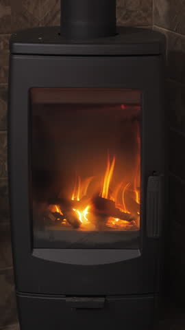 Warm orange flames dance in the fireplace, illuminating the cozy surroundings with a soft glow in a tranquil indoor setting at night. Vertical footage