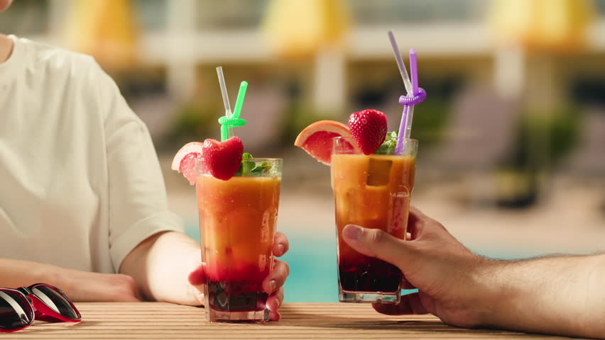 Fruit cocktail in hotel bar, Two cocktail glasses cheers in the hands on sea background. Bartenter making drink in bar, Summer vacation concept, A beautiful couple enjoy the vacation at the beach.