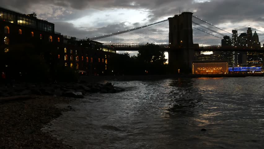 Brooklyn Bridge, New York City Manhattan downtown skyline cityscape, United States. Waterfront Pebble Beach, carousel in Dumbo, USA. Dramatic twilight dusk. Evening or night sky over dark riverfront.