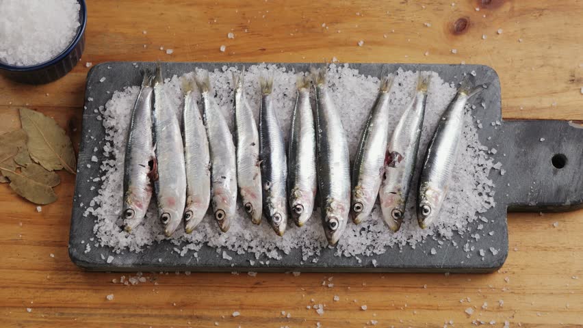 Chef cooking Fresh Sea sardines and Anchovy Fish and Mullus, salted fermented fish, On Display On Ice On Market Store Shop. Seafood Fish Background, sprats, smelt close up stand of small salty white