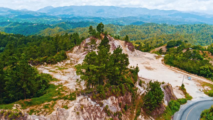 Picturesque mountain landscape under cloudy sky. Natural outdoor travel background. Scenery with green forests, blue hills and rocks. Ridge with high peak in the distance.