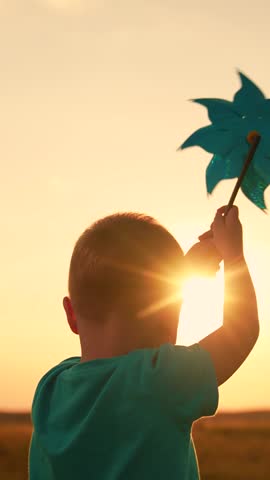 Kid playing with toy pinwheel in hand on summer field, sunny day. Childhood of boy. Happy child having fun with toy spinner outside in summer park. Family vacation, nature. Children outdoors. Baby sun