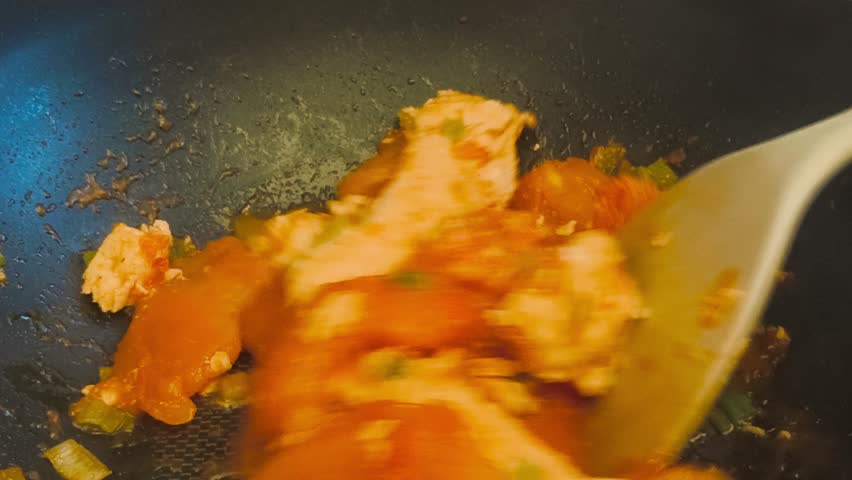 Close-up view of cooking hot, flavorful salmon with tomato sauce and sliced green onions in a sizzling frying pan on high heat. Indoor kitchen scene showcasing a delicious, freshly prepared meal.