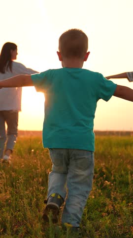 Mother daughter son running through meadow dreaming about flying to sky slow motion. Mom children having fun with raised hands dreaming in nature park. Family superhero game. Happy family silhouette