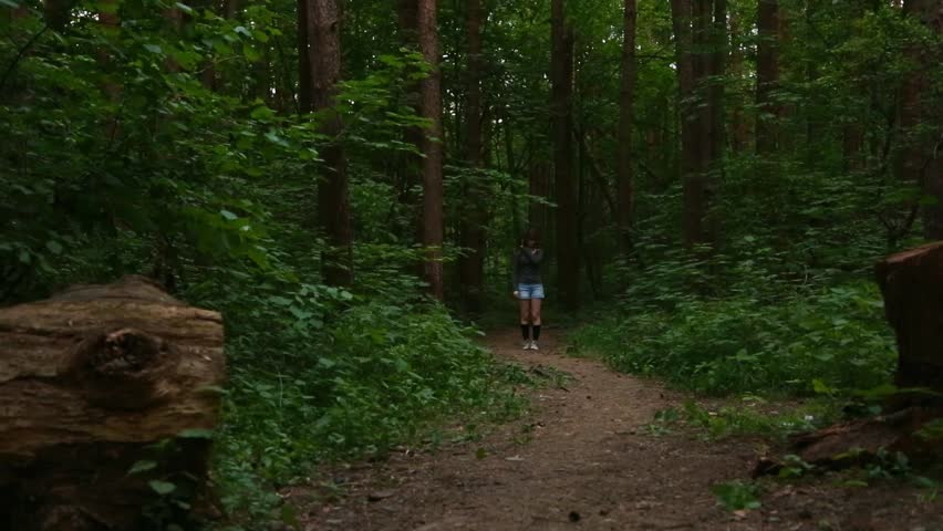 Beauty happy woman fast steps walking in sneakers on the path in pine green forest alone. Cute relax lady enjoying summer woods in sunny evening day. Model hiking in blue shorts. Full length