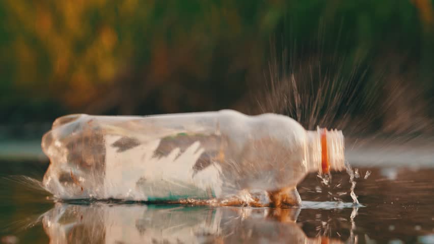 Plastic bottle falling into puddle with water splash slow motion environmental pollution concept at sunset - Powered by Shutterstock - Get 15% off with code: PIKWIZARD15