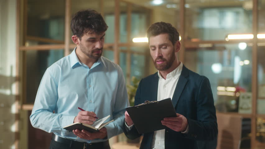 Professional businessmen adults Caucasian men co-workers partners discuss corporate documents analyze paperwork deal in office two male guys leader employee writing notes business plan consultation