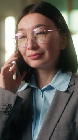 Smiling glad Asian businesswoman in office happy Korean Chinese Japanese woman business girl female entrepreneur building industry worker manager talk mobile phone smartphone call connection negotiate