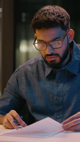 Indian businessman guy male entrepreneur writing document sign contract business deal on table in dark night office overwork Arabian man employee manager ceo write notes bank insurance loan paperwork