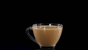 A sugar cube drops into a glass cup of tea, creating a dramatic splash against a black background - Powered by Shutterstock - Get 15% off with code: PIKWIZARD15