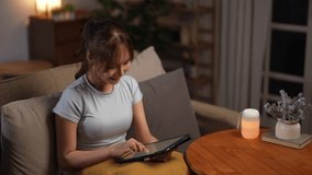 An Asian adult woman relaxes at home using a tablet for leisure reading an ebook or mobile app while practicing mental health and wellbeing in her daily routine. - Powered by Shutterstock - Get 15% off with code: PIKWIZARD15