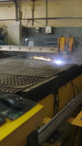 An industrial workshop features a precision laser cutter at work, creating intricate designs on metal. Sparks fly while smoke rises, showcasing advanced manufacturing technology.