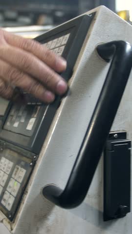 An operator is adjusting the controls on a complex piece of machinery in an industrial workshop. This activity takes place during the day, demonstrating skill and focus on the task.
