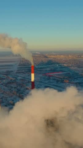 Smoke billows from industrial towers into the morning sky, casting shadows over a sprawling city. The scene highlights pollution's impact on urban living and the environment.