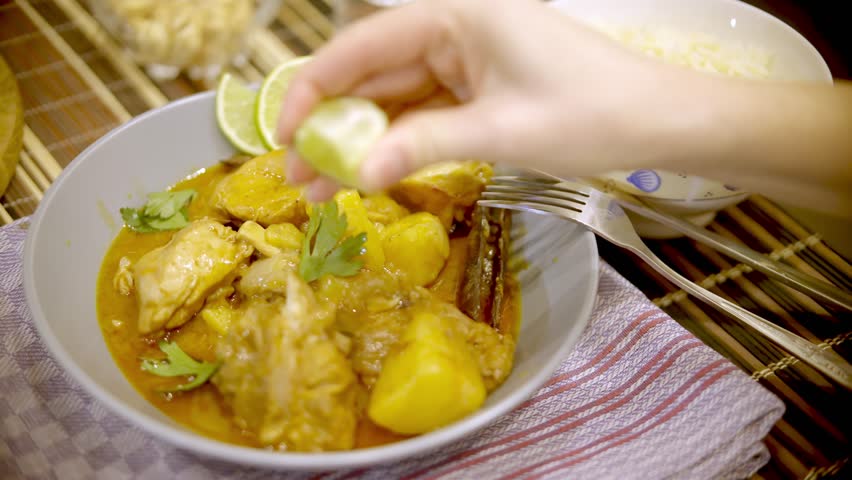 Hand squeezing lime over delicious chicken curry with potatoes. Fresh Homemade Stewed Chicken With Tikka Masala Sour Cream. Asia famous food. Chicken Dish in Pan. Thai chicken and peanut curry
